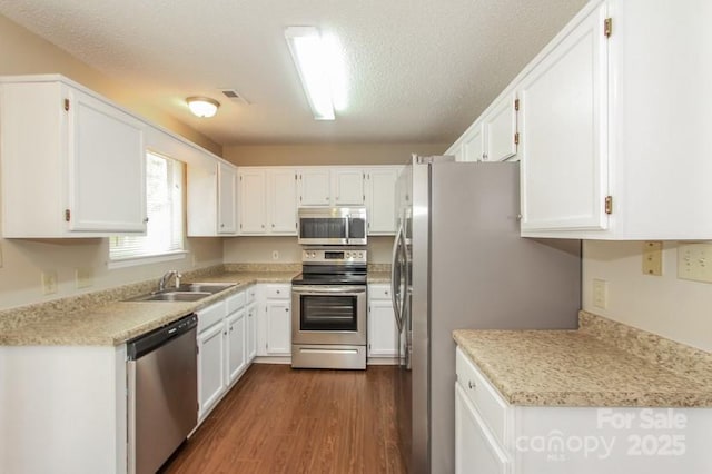 kitchen with appliances with stainless steel finishes, dark wood-type flooring, a sink, and white cabinetry