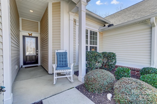 view of exterior entry featuring covered porch and roof with shingles