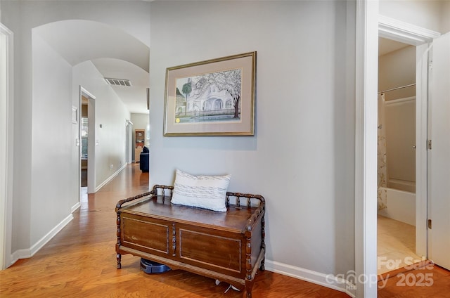 hall featuring arched walkways, visible vents, light wood-style flooring, and baseboards