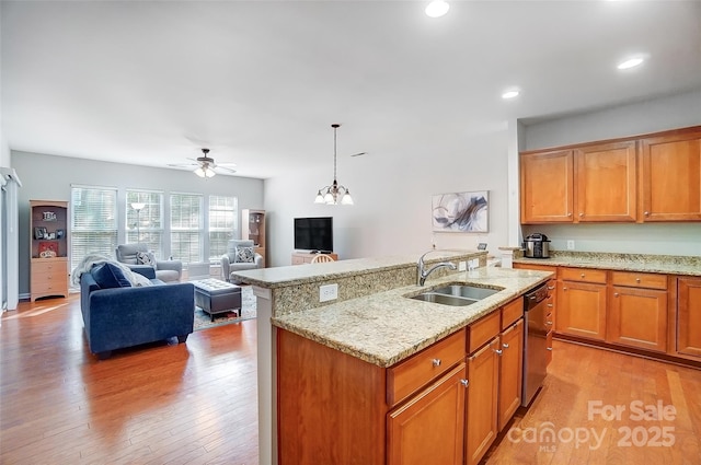 kitchen with light wood-type flooring, dishwasher, light stone counters, and a sink