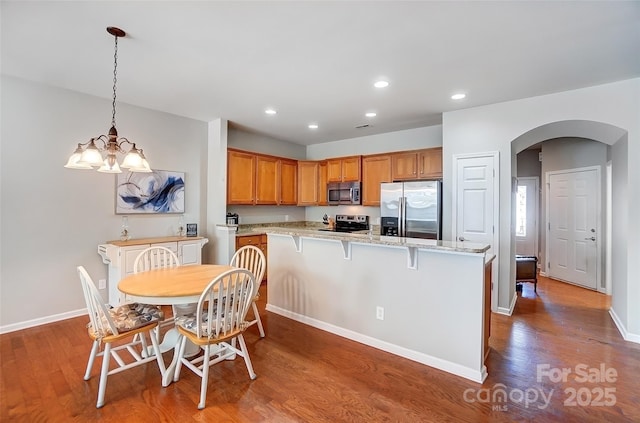 kitchen with arched walkways, brown cabinets, wood finished floors, stainless steel appliances, and pendant lighting