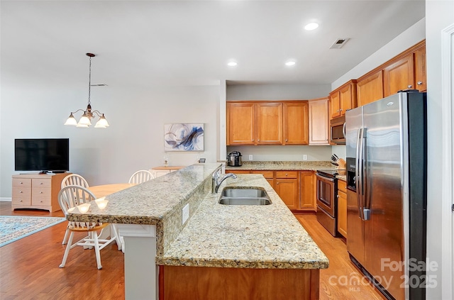 kitchen featuring a breakfast bar area, stainless steel appliances, visible vents, light wood-style floors, and a sink