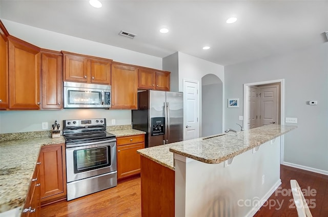 kitchen with arched walkways, appliances with stainless steel finishes, and brown cabinets