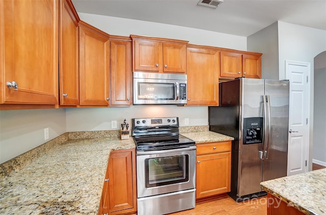 kitchen with arched walkways, stainless steel appliances, brown cabinetry, and visible vents