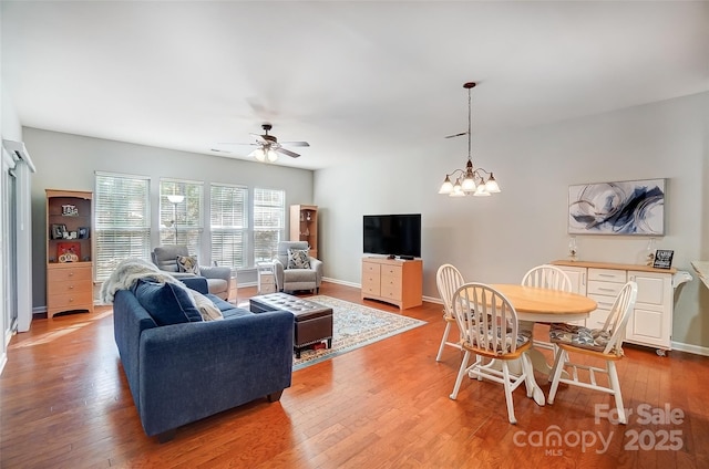 living room featuring baseboards, light wood finished floors, and ceiling fan with notable chandelier