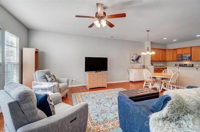 living area featuring light wood-style flooring, recessed lighting, ceiling fan with notable chandelier, visible vents, and baseboards