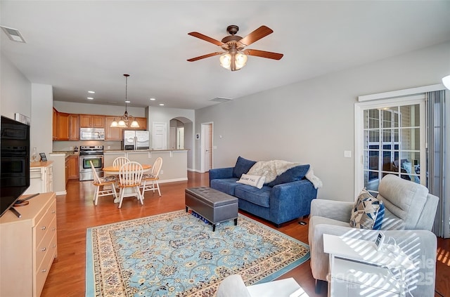 living room with arched walkways, light wood-style flooring, ceiling fan with notable chandelier, and visible vents