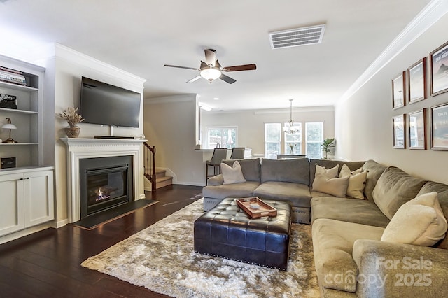 living room featuring dark wood-type flooring, a ceiling fan, visible vents, a glass covered fireplace, and crown molding