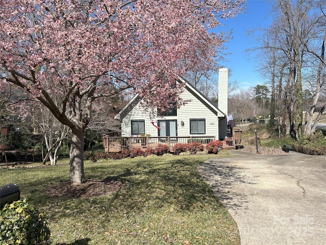 view of front of house with a front yard, a chimney, driveway, and a wooden deck