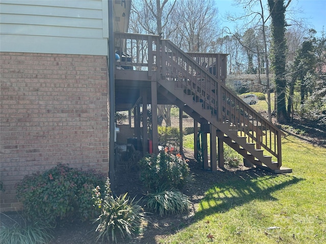 view of home's exterior with brick siding, a deck, stairs, and a yard