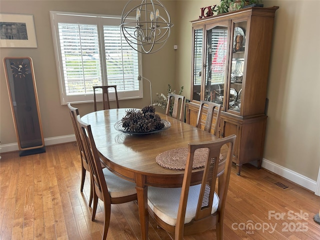 dining space featuring baseboards, a notable chandelier, and light wood finished floors