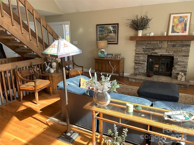 living area featuring a stone fireplace, stairway, wood finished floors, and baseboards