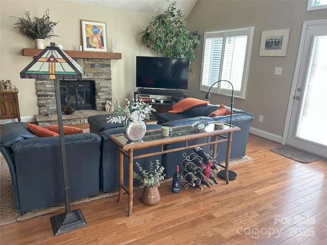 living area featuring a stone fireplace, baseboards, lofted ceiling, and wood finished floors