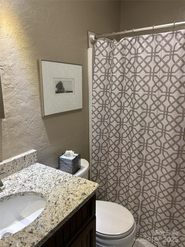 bathroom featuring a shower with shower curtain, toilet, vanity, and a textured wall