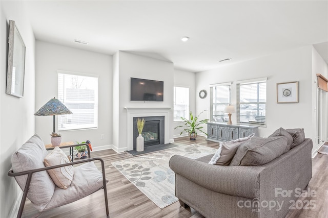 living room with wood finished floors, a glass covered fireplace, visible vents, and baseboards