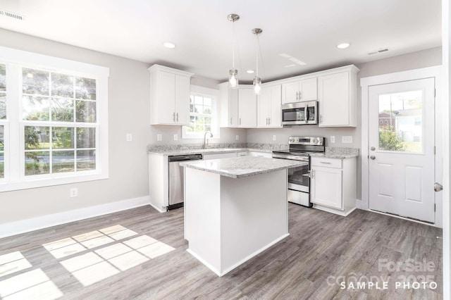kitchen featuring stainless steel appliances, a center island, visible vents, white cabinetry, and wood finished floors