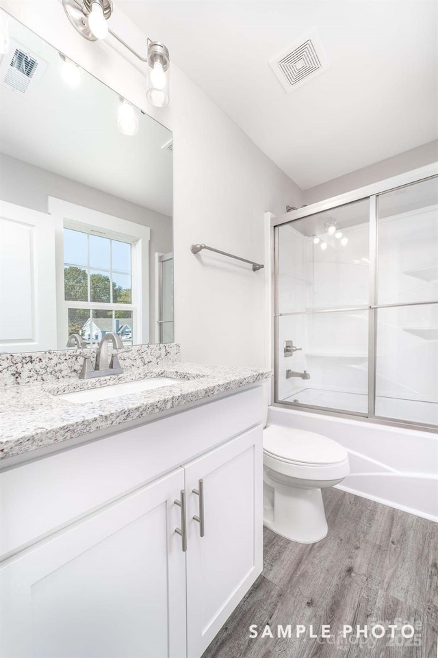 bathroom featuring bath / shower combo with glass door, wood finished floors, visible vents, and vanity