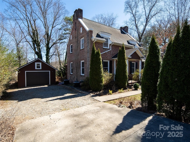 view of front of house with an outbuilding, brick siding, a detached garage, a chimney, and driveway