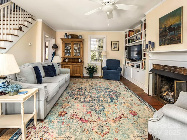 living room featuring stairway, crown molding, a stone fireplace, and ceiling fan