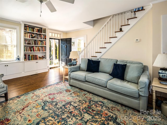 living room with ceiling fan, wood finished floors, visible vents, stairway, and crown molding