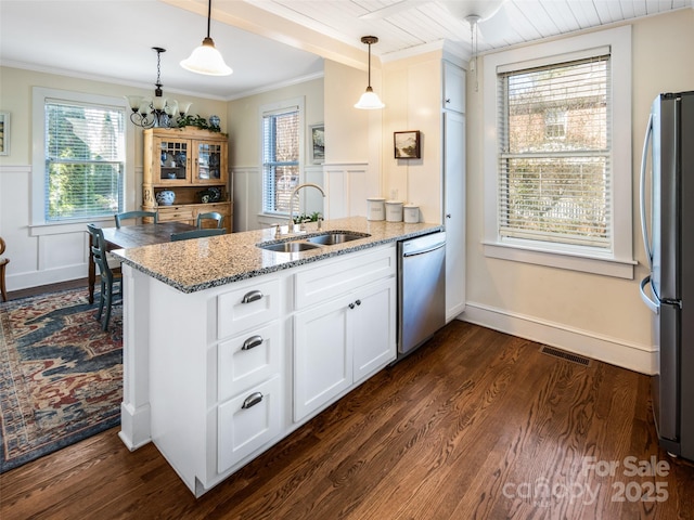 kitchen with appliances with stainless steel finishes, white cabinetry, a sink, light stone countertops, and a peninsula