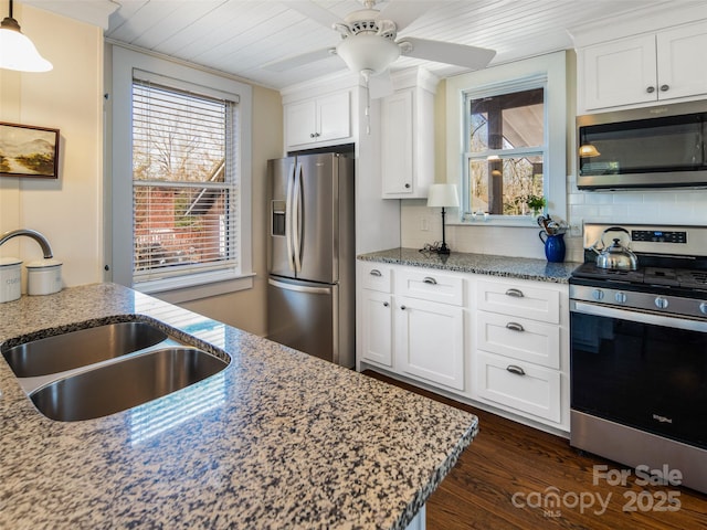 kitchen with light stone counters, stainless steel appliances, decorative backsplash, white cabinetry, and a sink