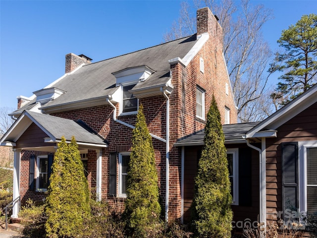 view of home's exterior with a shingled roof, a chimney, and brick siding