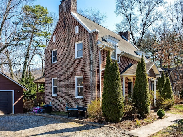 view of side of property with brick siding, a chimney, an outdoor structure, and central air condition unit