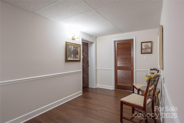 hallway featuring baseboards, a drop ceiling, and wood finished floors