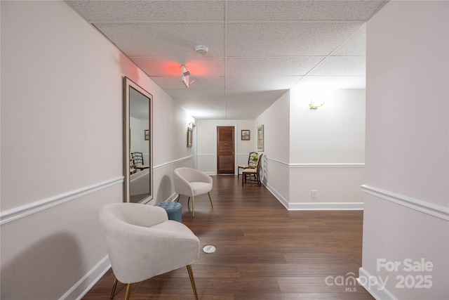 sitting room featuring a drop ceiling, baseboards, and wood finished floors