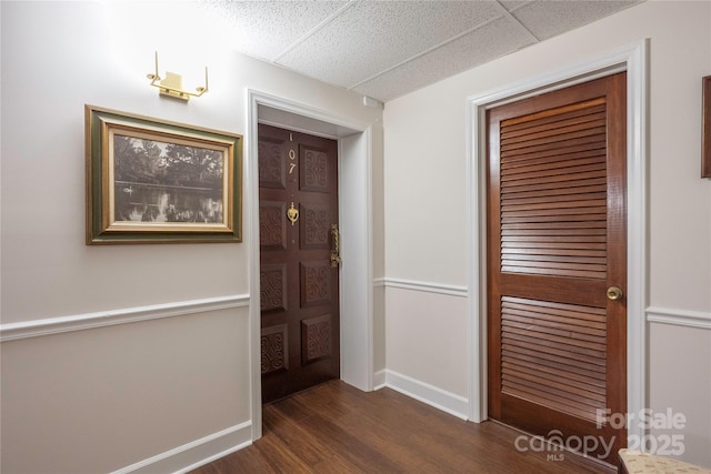 interior space with dark wood finished floors, a paneled ceiling, and baseboards