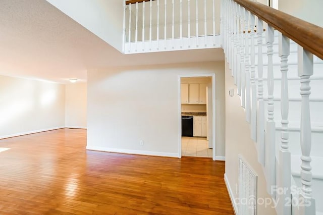 interior space featuring hardwood / wood-style flooring, a towering ceiling, visible vents, stairs, and baseboards