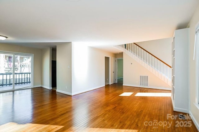 unfurnished living room featuring wood-type flooring, stairs, visible vents, and baseboards