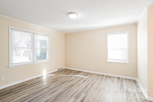 empty room with ornamental molding, a wealth of natural light, light wood-style flooring, and baseboards