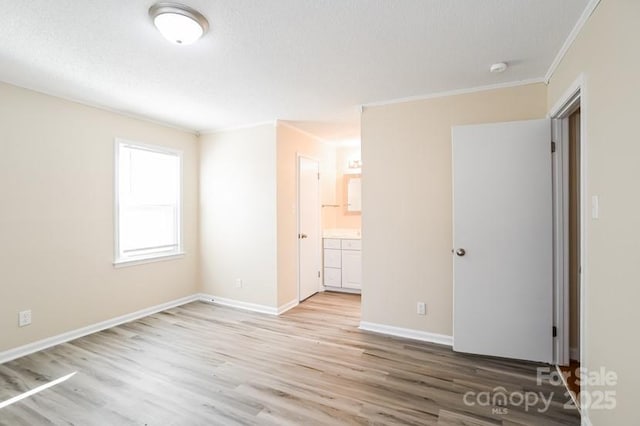 unfurnished bedroom with crown molding, light wood finished floors, ensuite bathroom, a textured ceiling, and baseboards