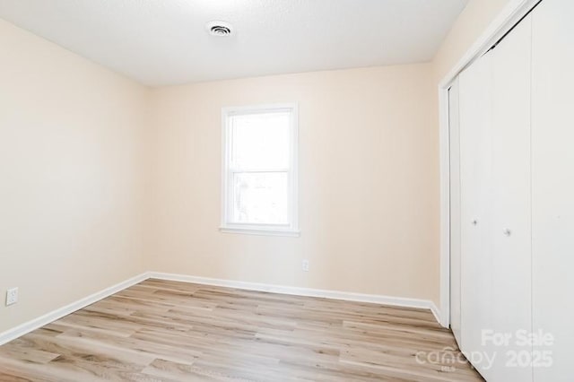 unfurnished bedroom featuring light wood-style flooring, visible vents, baseboards, and a closet