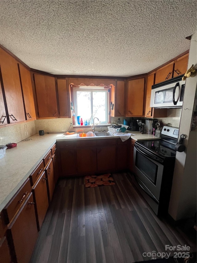 kitchen featuring brown cabinetry, dark wood-style flooring, stainless steel appliances, light countertops, and a sink