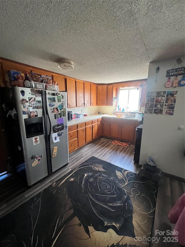 kitchen featuring brown cabinetry, stainless steel fridge with ice dispenser, wood finished floors, light countertops, and a sink