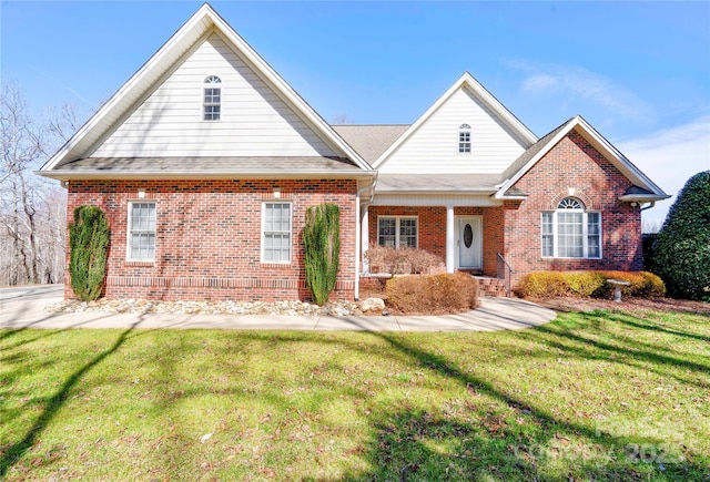 view of front of home with a shingled roof, a front lawn, and brick siding