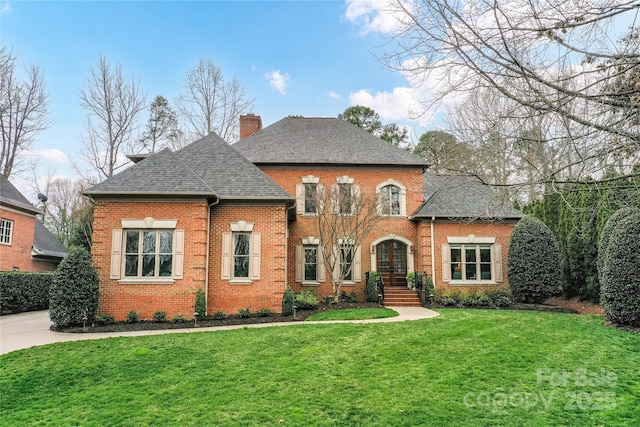 colonial inspired home with a front lawn, brick siding, roof with shingles, and a chimney