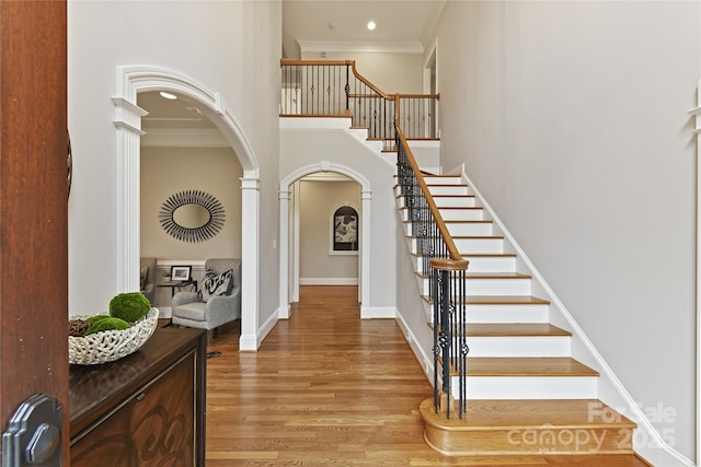 entryway featuring baseboards, arched walkways, ornamental molding, and light wood finished floors