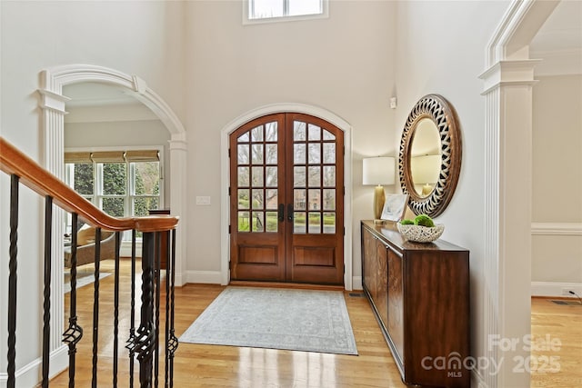 foyer entrance with light wood-type flooring, visible vents, french doors, arched walkways, and baseboards