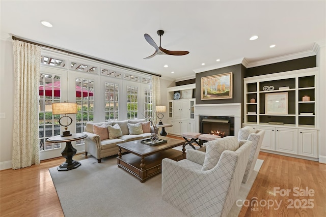 living area featuring a high end fireplace, light wood finished floors, crown molding, and ceiling fan