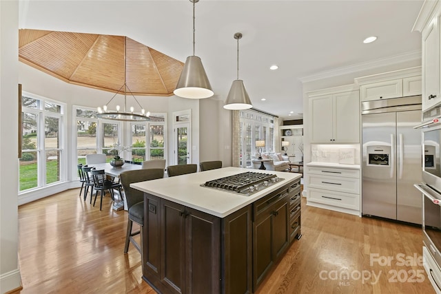 kitchen featuring stainless steel appliances, light countertops, white cabinets, a kitchen bar, and light wood-type flooring