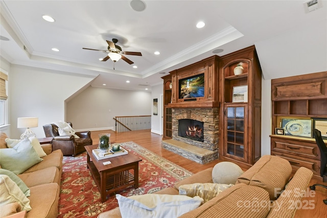 living area with visible vents, a tray ceiling, wood finished floors, a fireplace, and crown molding