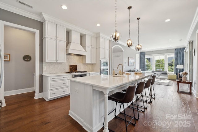 kitchen with dark wood finished floors, stainless steel appliances, visible vents, white cabinets, and premium range hood