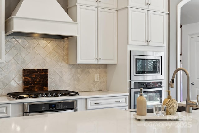 kitchen featuring stainless steel appliances, white cabinets, light countertops, decorative backsplash, and custom range hood