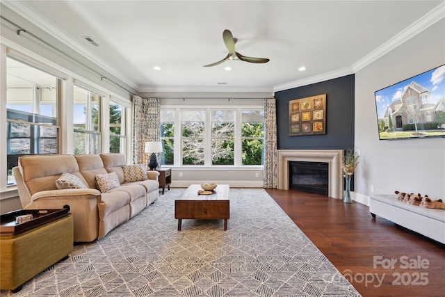 living area featuring visible vents, a glass covered fireplace, ceiling fan, ornamental molding, and wood finished floors