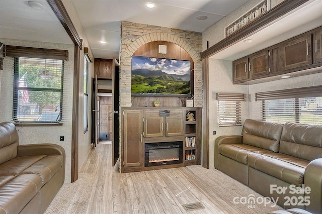 living area featuring a glass covered fireplace, visible vents, and light wood finished floors