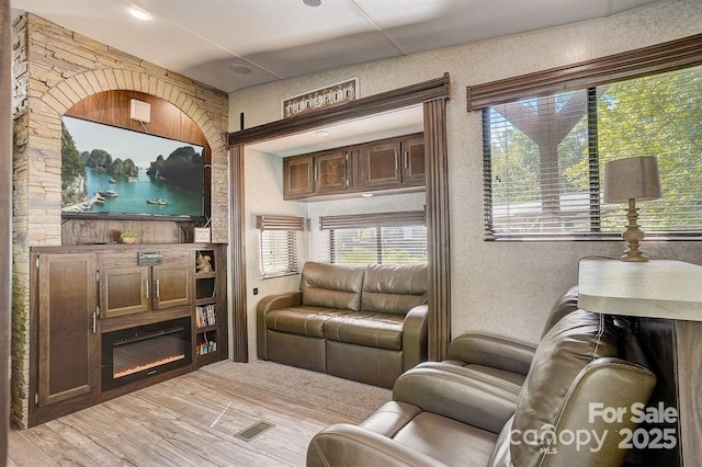 living area with light wood-style floors, visible vents, and a glass covered fireplace